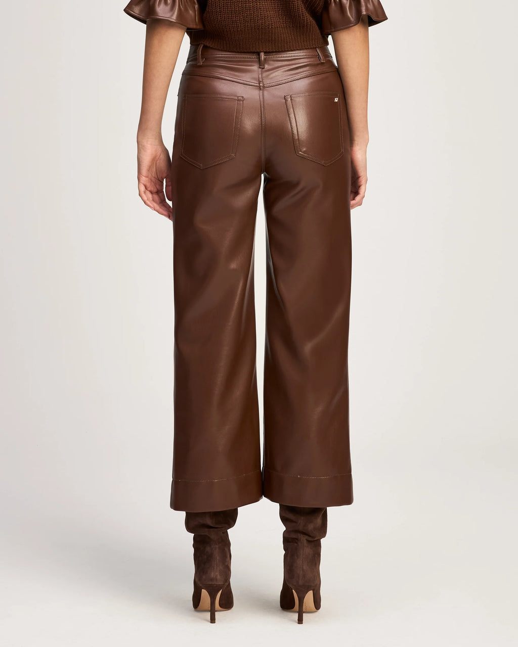 Back view of a model wearing the Cinq à Sept Joey vegan leather pant in Espresso, highlighting the denim-inspired back pockets and cropped hem.