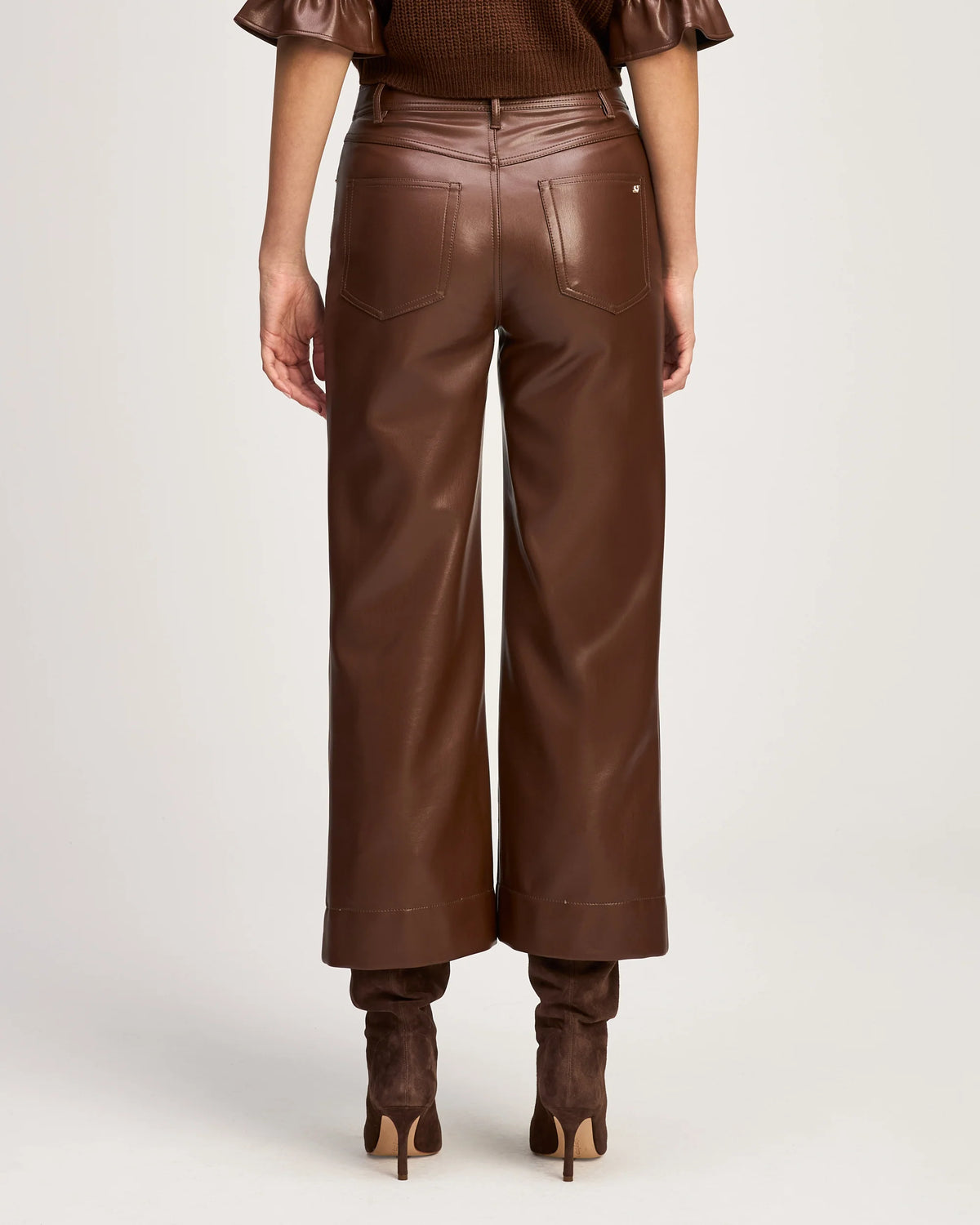 Back view of a model wearing the Cinq à Sept Joey vegan leather pant in Espresso, highlighting the denim-inspired back pockets and cropped hem.