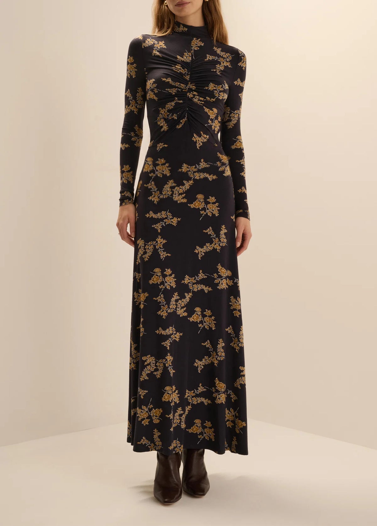 Front view of a woman wearing the Favorite Daughter Lucia high-neck, long-sleeve maxi dress in navy vine floral print without a belt, paired with dark brown ankle boots.