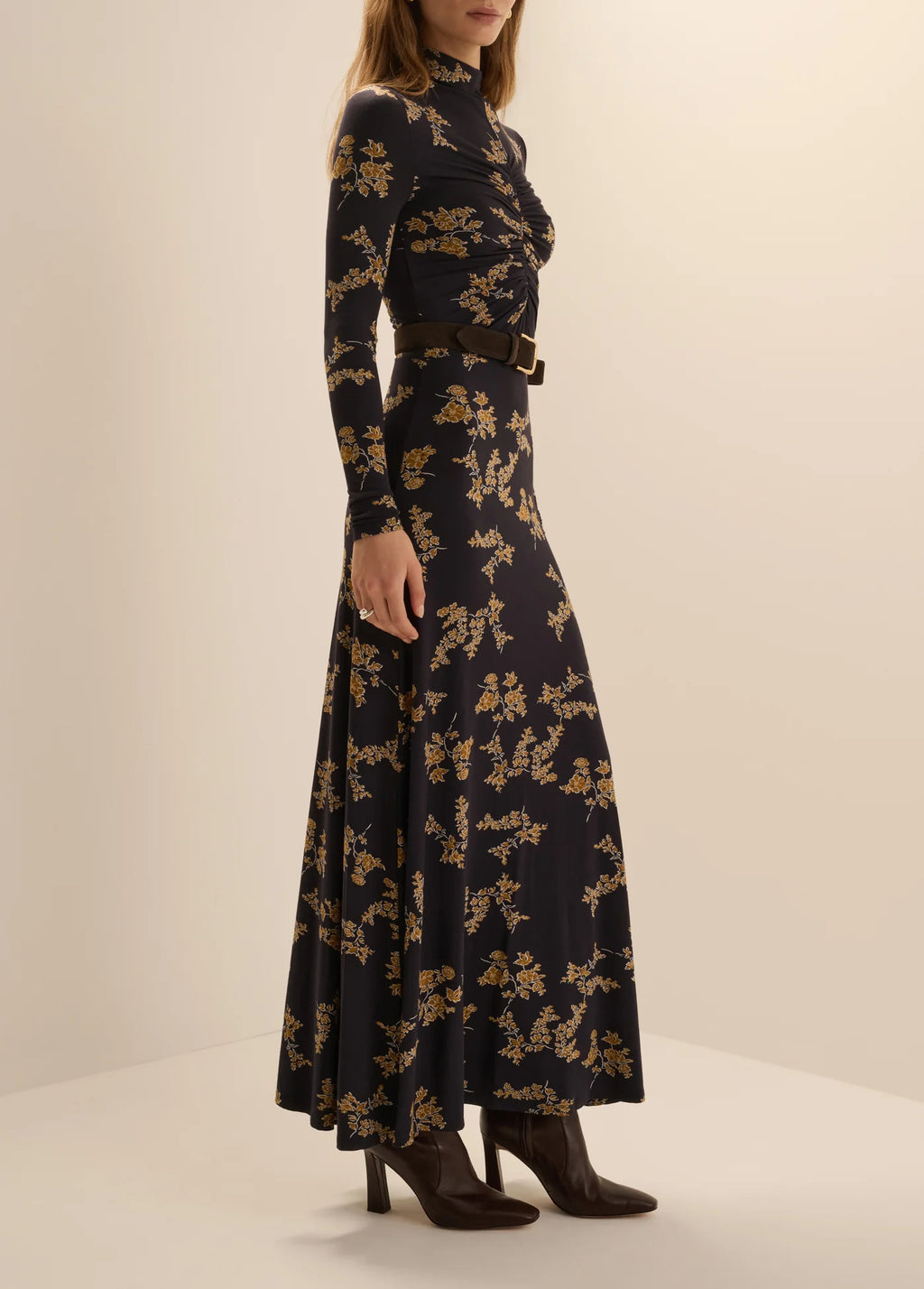 A woman wearing the Favorite Daughter Lucia long-sleeve, high-neck maxi dress in navy vine floral print, styled with a black belt and dark brown ankle boots.